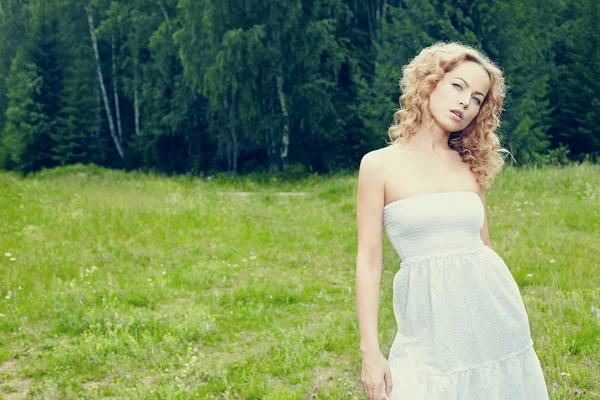 Hermosa chica rubia en el campo verde con flores. Escena rural —  Fotos de Stock