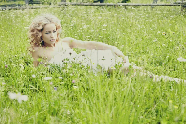 Menina loira bonita no campo verde com flores. Cena rural — Fotografia de Stock