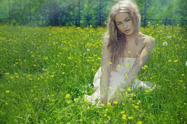 Beautiful blond girl on green field with flowers. Rural scene