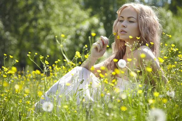美丽的金发女孩用鲜花绿色领域。农村现场 — 图库照片