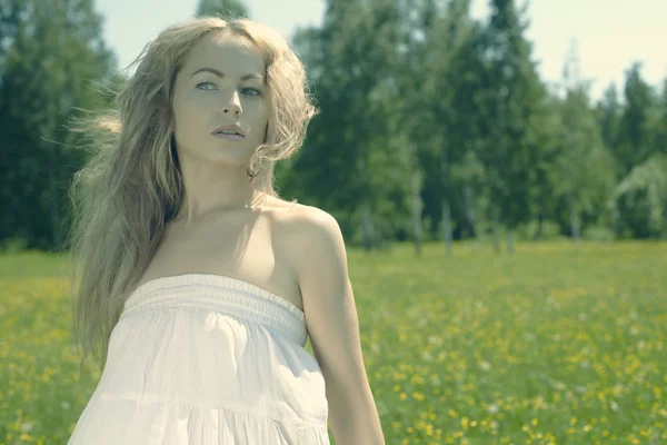 Beautiful blond girl on green field with flowers — Stock Photo, Image