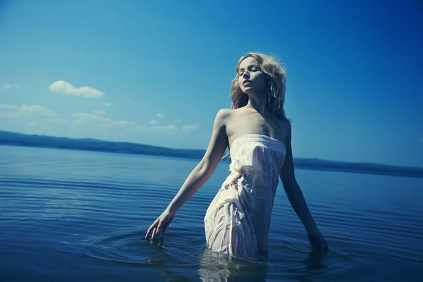 Mladá sexy blondýna v modré vodě v mokré bílé šaty — Stock fotografie