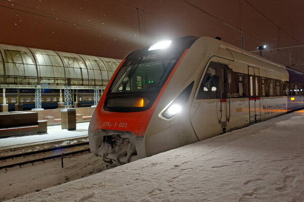 Харьков, Украина - 28 января 2022 года: Пассажирский поезд железной дороги ДПКр-3 отправляется со станции платформы на Харьковском пассажирском вокзале. Ночное фото.
