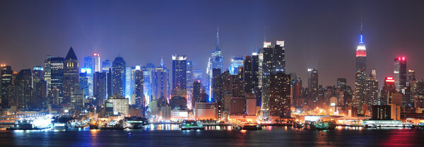 New York City Manhattan midtown skyline at night with skyscrapers lit over Hudson River with reflections.