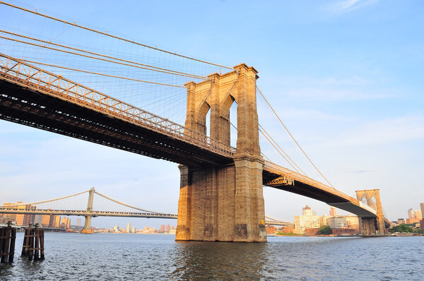 Brooklyn Bridge over East River viewed from New York City Lower Manhattan waterfront at sunset.