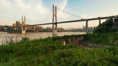 Chongqing şehri zaman çizelgesi. Gün batımından batımına kadar şehir merkezindeki gökdelen ve Çin nehri üzerindeki köprü manzarası.