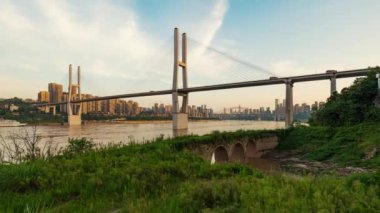 Chongqing şehri zaman çizelgesi. Gün batımından batımına kadar şehir merkezindeki gökdelen ve Çin nehri üzerindeki köprü manzarası.