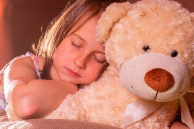 Tatlı rüyalar. Mutlu, küçük, güzel bir kızın portresi arkadaşı oyuncak ayının yanında uyuyakalıyor. Mutlu tasasız çocukluk, aile ve ev kavramı. 