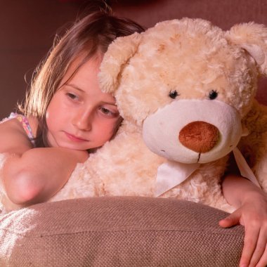 Çocukların korku ve endişe konsepti. Evinde oyuncak ayısına sarılan üzgün küçük bir kızın portresi.. 