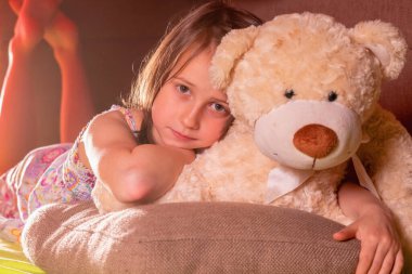 Çocukların korku ve endişe konsepti. Evinde oyuncak ayısına sarılan üzgün küçük bir kızın portresi. Yatay resim.