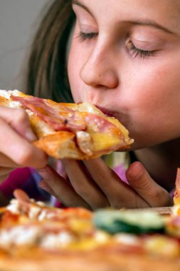 Yakından genç ve çekici bir kız lezzetli bir dilim pizzanın tadını çıkarıyor. Seçici odaklanma. Dikey resim.