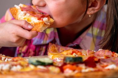 Genç ve çekici bir kız lezzetli bir dilim pepperonili pizzanın tadını çıkarıyor. Yatay resim.