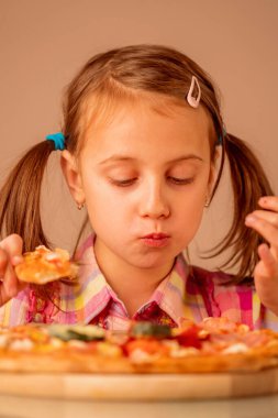 Genç kız lezzetli bir dilim pizzayı seviyor, bu tadı seviyor, zevkten gözlerini kapıyor, iştahı yerinde. Dikey resim.