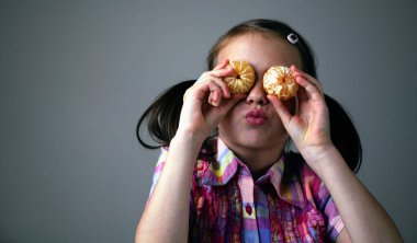 Genç, güzel, mutlu bir kızın komik portresi mandalinayı iki gözünün içine yerleştirir. Uzayı kopyala Yatay resim.