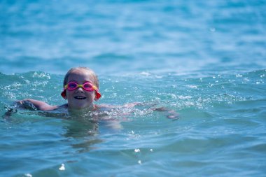 Genç güzel kız denizde eğleniyor. Neşeli çocuk dalgalarda yüzüyor. Seyahat, aktiviteler ve tatil konsepti. Boşluğu kopyala.