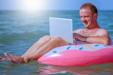 Her yerden çalışma ve uzaktan işgal konsepti. Denizdeki şişirilebilir halka üzerinde dizüstü bilgisayarla çalışan iş adamı portresi. 