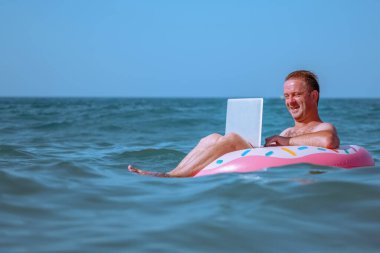 Her yerden çalışma ve uzaktan işgal konsepti. Mavi denizdeki şişme halkada dizüstü bilgisayarla çalışan mutlu iş adamı portresi. Boşluğu kopyala.