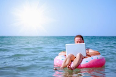 Her yerden çalışma ve uzaktan işgal konsepti. İş adamı serbest yazar, Tropikal Denizde şişme halka üzerine dizüstü bilgisayarla çalışıyor. Boşluğu kopyala.