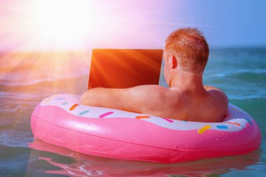 Her yerden çalışma ve uzaktan işgal konsepti. Tropik denizdeki şişme halka üzerinde dizüstü bilgisayarla çalışan iş adamının portresi. 