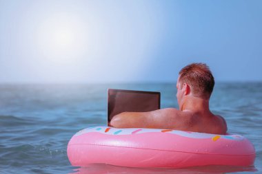 Her yerden çalışma ve uzaktan işgal konsepti. Tropikal denizde dizüstü bilgisayarla şişme halka üzerinde çalışan iş adamının portresi. Boşluğu kopyala.