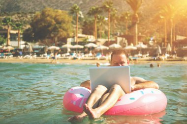 Her yerden ve her zaman çalış. İş adamı serbest yazar, Tropikal Denizde şişme halka üzerine dizüstü bilgisayarla çalışıyor. Boşluğu kopyala.