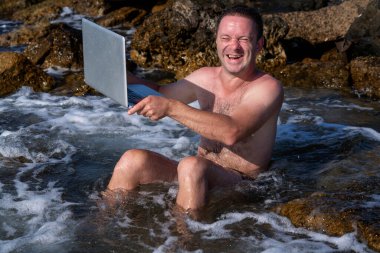 Bilgisayar defterini temizleme işleminin komik bir görüntüsü. Genç adam denizde tatilde dizüstü bilgisayarla çalışıyor.. 