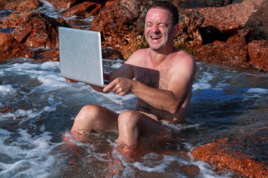 Bilgisayar defterini temizleme işleminin komik bir görüntüsü. Genç bir adamın denizde dizüstü bilgisayarla çalışmasının komik bir görüntüsü. Yatay resim.