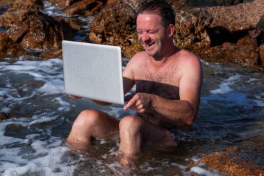 Bilgisayar defterini temizleme işleminin komik bir görüntüsü. Genç bir adamın denizde dizüstü bilgisayarla çalışmasının komik bir görüntüsü..