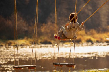 Güzel bir genç kız dışarıda salıncakta nehri ve dağları aşıp eğleniyor. Yatay görüntü. Boşluğu kopyala.