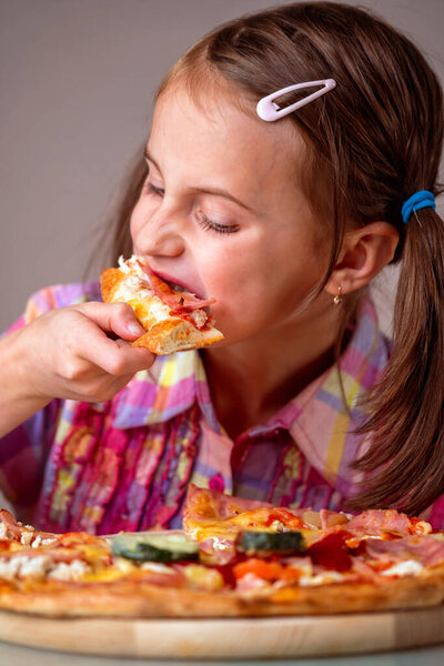 Young beautiful attractive girl enjoys delicious slice of  pepperoni pizza. Hungry female child indoor