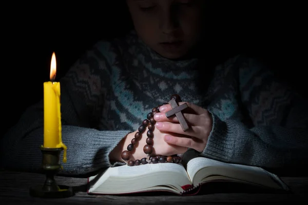 木製のロザリオとろうそくの光の中で聖書を読んで神に祈る若い美しい女の子 クロスに焦点を当てる — ストック写真