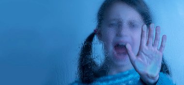 Kavramsal imaj: Çocukları ve reşit olmayan gençleri şiddet, istismar, istismar ve ihmalden korumak. Islak camın arkasından dur işareti yapan genç bir kız. Elimizdeki seçici odaklanma. Boşluğu kopyala.