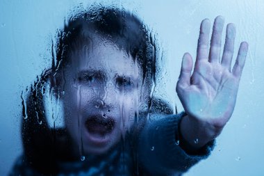 Kavramsal imaj: Çocukları ve reşit olmayan gençleri şiddet, istismar, istismar ve ihmalden korumak. Islak camın arkasından dur işareti yapan genç bir kız. Eldeki seçici odaklanma.