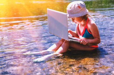 Güneş ışınları altında dizüstü bilgisayarla çalışan mutlu bir genç kız. Serbest iş, seyahat, tatiller, bağlı kalmak, online çalışmak, e-öğrenim kavramı. Boşluğu kopyala