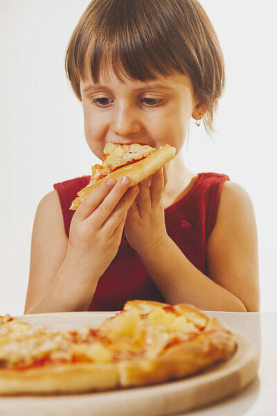 Beautiful child girl enjoys delicious slice of pizza, likes this taste, she has good appetite. Vertical image