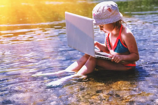 Güneş ışınları altında dizüstü bilgisayarla çalışan mutlu bir genç kız. Serbest iş, seyahat, tatiller, bağlı kalmak, online çalışmak, e-öğrenim kavramı. Boşluğu kopyala