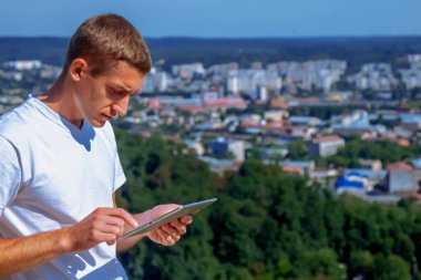 Her yerde ve her zaman çalışıyorum. Tablet kullanan yakışıklı işadamının portresi ve şehrin panoramik manzarasına karşı uzaktan çalışma.. 
