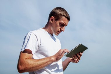 Her yerde ve her zaman çalışıyorum. Tablet kullanan ve mavi gökyüzünün arka planına karşı uzaktan çalışan yakışıklı bir iş adamı.. 