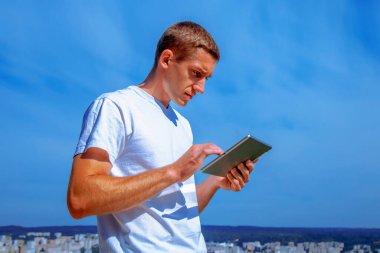 Şehir ve mavi gökyüzünün tabletini kullanan yakışıklı bir iş adamı. Tasarım için alanı kopyala. 