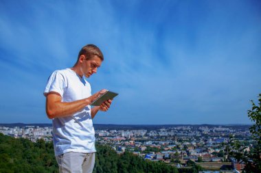 Şehrin panoramik manzarasının arka planına karşı tablet kullanan yakışıklı bir işadamı. Tasarım için alanı kopyala.