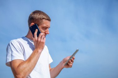 Yakışıklı genç işadamı elinde aletle mavi gökyüzünün arka planına karşı tablet kullanıyor. Tasarım için alanı kopyala.