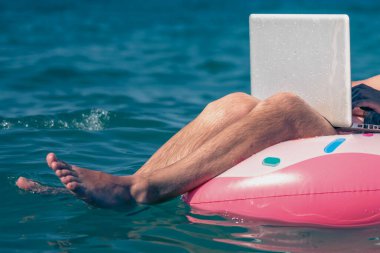 Her yerde ve her zaman çalışmak. Dizüstü bilgisayarla denizde şişme halka üzerinde çalışan serbest çalışan bir adam. Seçici odak.