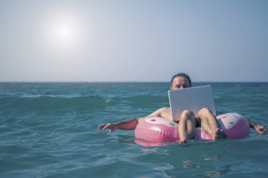 Adam denizdeki bir dizüstü bilgisayarda çalışıyor. Eğlence ve uzaktan çalışma kavramı. 