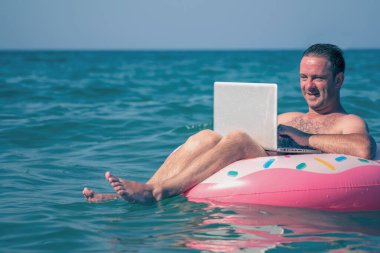 Adam denizdeki bir dizüstü bilgisayarda çalışıyor. Eğlence ve uzaktan çalışma konsepti. Boşluğu kopyala.