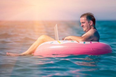 Her yerde ve her zaman çalışmak. Sudaki şişme halka üzerinde dizüstü bilgisayar kullanan genç bir adam çalışıyor. Serbest çalışma, tatiller, mesai