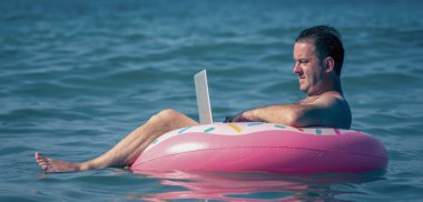 Denizde tatilde uzaktan çalışma. İşadamı, okyanusun sularında şişme halka üzerine bir dizüstü bilgisayarla çalışıyor.. 