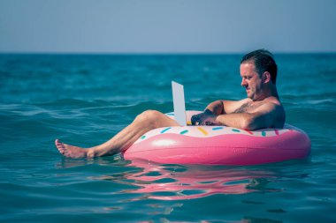 Denizde tatilde uzaktan çalışma. Okyanus suyunda dizüstü bilgisayarı olan bir adam. Yatay resim.