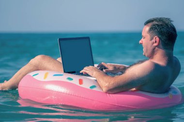 İşadamı çalışıyor. Sudaki şişme halka üzerinde dizüstü bilgisayar kullanıyor..