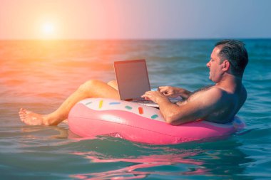 Deniz ya da okyanus suyunda şişme halka üzerine dizüstü bilgisayarı olan bir iş adamı.