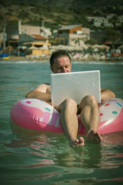 Deniz suyunda şişme halkası olan serbest çalışan bilgisayar üzerinde çalışır. Silber gri dizüstü bilgisayarı olan, yüzme çemberindeki Huppy adam.. 